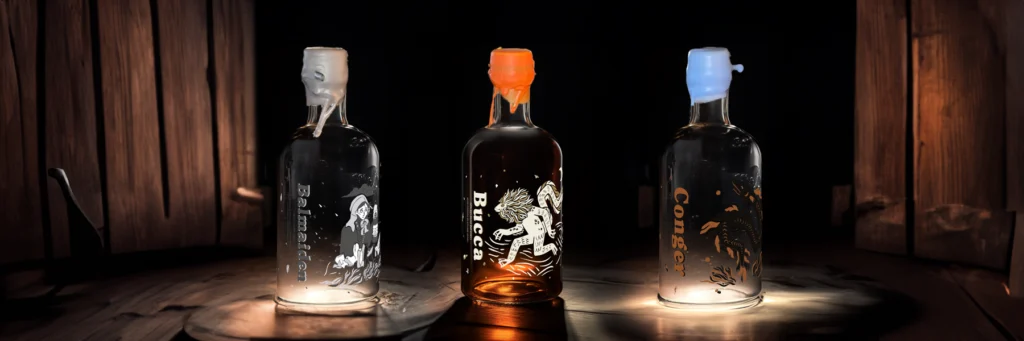 Three bottles of Bal Maiden Gin, Bucca Rum, and Conger Vodka illuminated on a rustic wooden surface, with a warm, ambient light highlighting their intricate designs against a dark background.